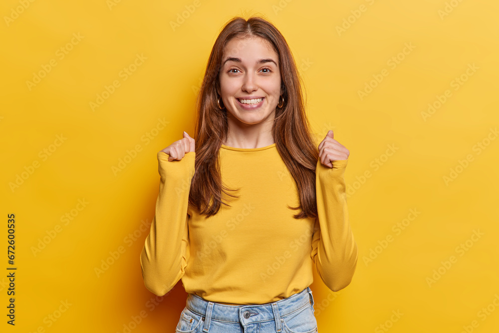 Positive European woman hopes for good luck clenches fists has big expectations for something nice happen dressed in casual clothing isolated over vivid yellow background. People wish desire concept Positive European woman hopes for good luck clenches fists has big expectations for something nice happen dressed in casual clothing isolated over vivid yellow background. People wish desire concept