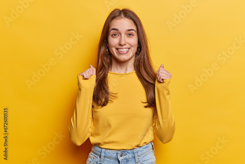 Positive European woman hopes for good luck clenches fists has big expectations for something nice happen dressed in casual clothing isolated over vivid yellow background. People wish desire concept