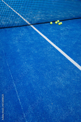 blue paddle tennis court net with five balls nearby, racket sports concept © Vic