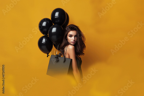 Femme brune et jeune avec une robe noire portant un sac de shopping sur l'épaule et des ballons baudruches noirs sur un fond jaune moutarde. Shopping, black Friday, Soldes