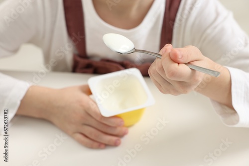 Cute little girl with tasty yogurt at white table, closeup