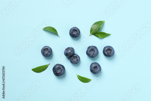 Tasty fresh blueberries with green leaves on light blue background, flat lay
