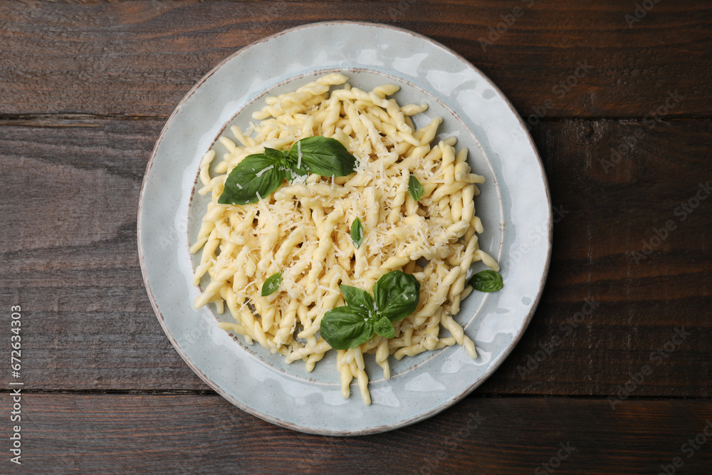 Plate of delicious trofie pasta with cheese and basil leaves on wooden table, top view