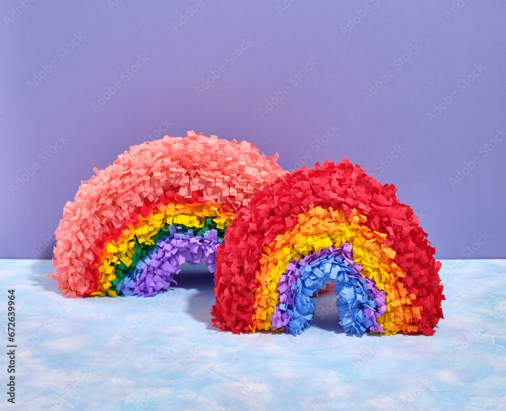Theme of celebration and fun. Two festive multicolored rainbow pinatas stand on a purple colorful background. Birthday composition.
