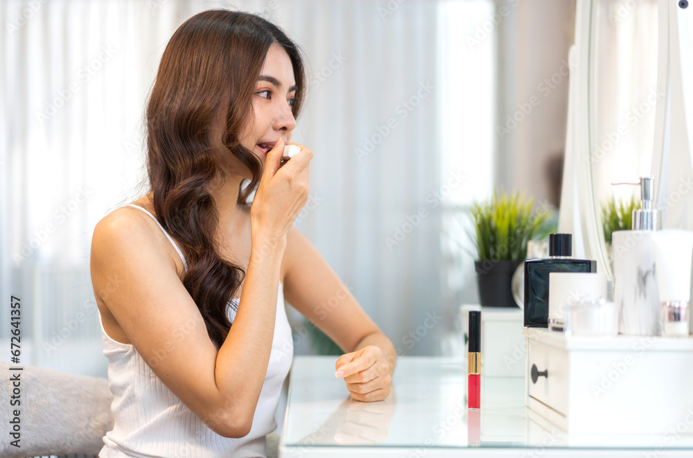 Smiling beautiful asian woman fresh healthy skin looking on mirror and enjoying applying skincare lips with red lipstick at home.facial beauty and cosmetic concept Smiling beautiful asian woman fresh healthy skin looking on mirror and enjoying applying skincare lips with red lipstick at home.facial beauty and cosmetic concept