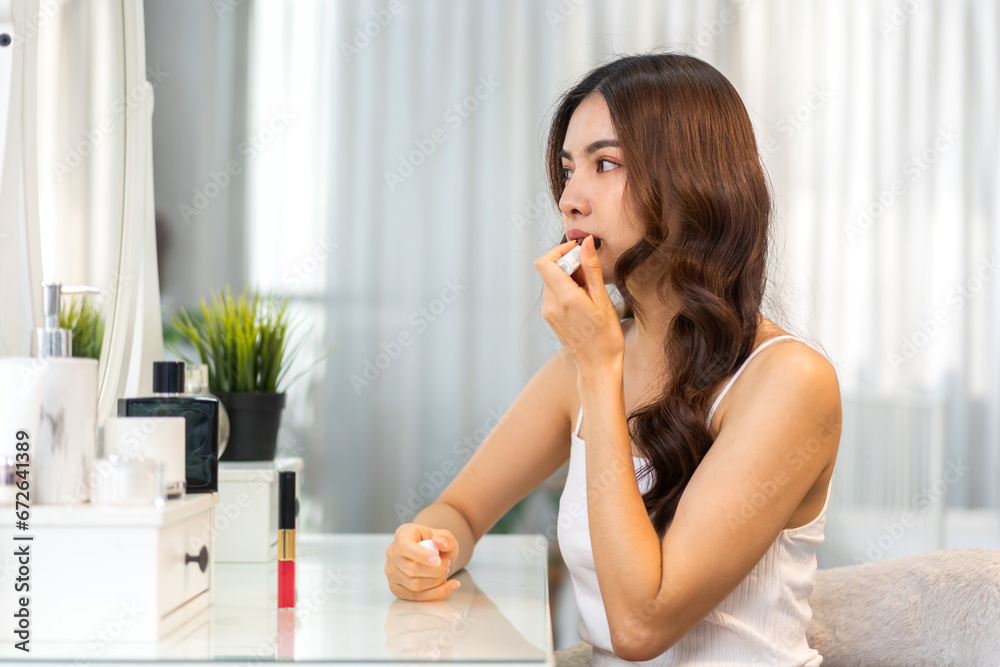 Smiling beautiful asian woman fresh healthy skin looking on mirror and enjoying applying skincare lips with red lipstick at home.facial beauty and cosmetic concept Smiling beautiful asian woman fresh healthy skin looking on mirror and enjoying applying skincare lips with red lipstick at home.facial beauty and cosmetic concept
