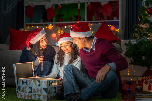 Portrait of happy family father and mother with daughter in santa hats having fun opening magic christmas gift box and enjoying spending time together in christmas time at home © Art_Photo