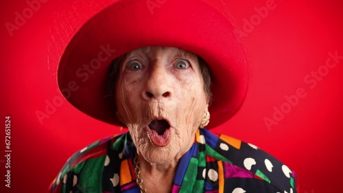 Saying WOW, a happy fisheye portrait caricature of funny elderly woman with red hat isolated on red background. photo