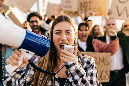 Large group of diverse people manifesting against war or attack on a country. Female activist using megaphone outdoors. Stop war signs and banners in a peace demonstration photo