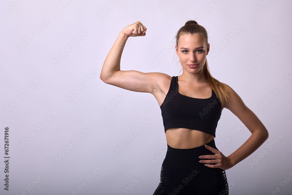 Happy confident young charming woman raising her hand clenched fist, showing biceps. Champion sports slender cute girl showing pumped up body and arms Happy confident young charming woman raising her hand clenched fist, showing biceps. Champion sports slender cute girl showing pumped up body and arms