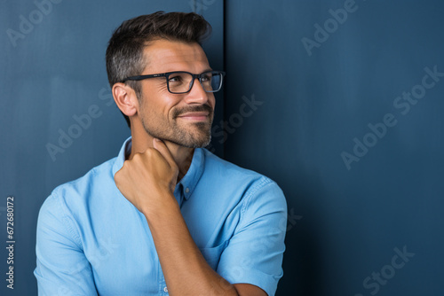Summer portrait of confident, handsome man wearing blue shirt and glasses, looking away with hand on chin, Side view, Studio shot