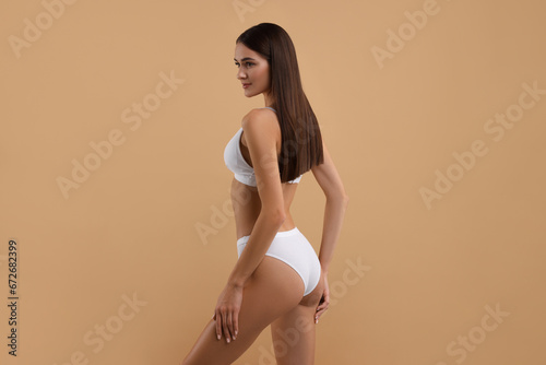 Young woman in stylish white bikini on beige background