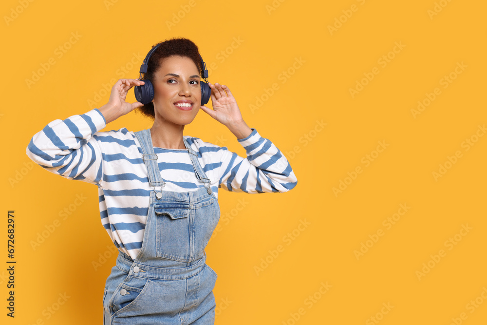 Happy young woman in headphones dancing on orange background. Space for text Happy young woman in headphones dancing on orange background. Space for text