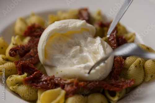 Closeup of pesto conchiglie with sundried tomatoes and cutting burrata cheese served in white plate