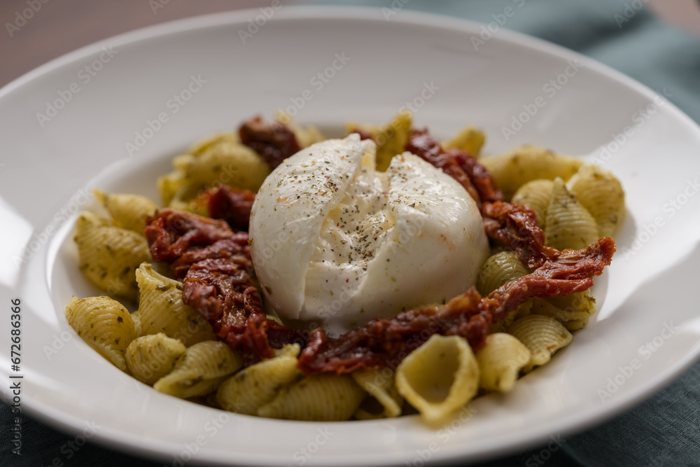 Closeup of pesto conchiglie with sundried tomatoes and burrata cheese served in white plate
