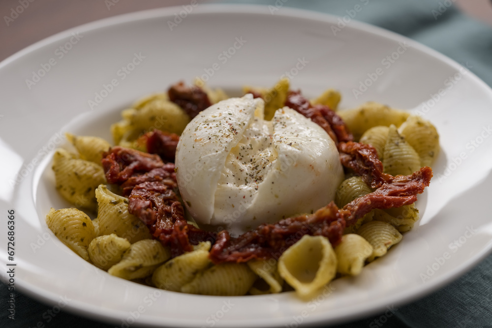 Closeup of pesto conchiglie with sundried tomatoes and burrata cheese served in white plate Closeup of pesto conchiglie with sundried tomatoes and burrata cheese served in white plate