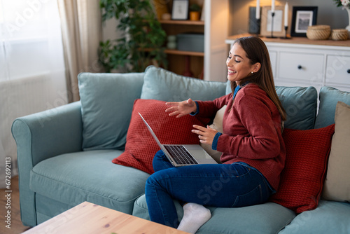 Happy female entrepreneur sitting on sofa and sharing ideas over online meeting on laptop at home.