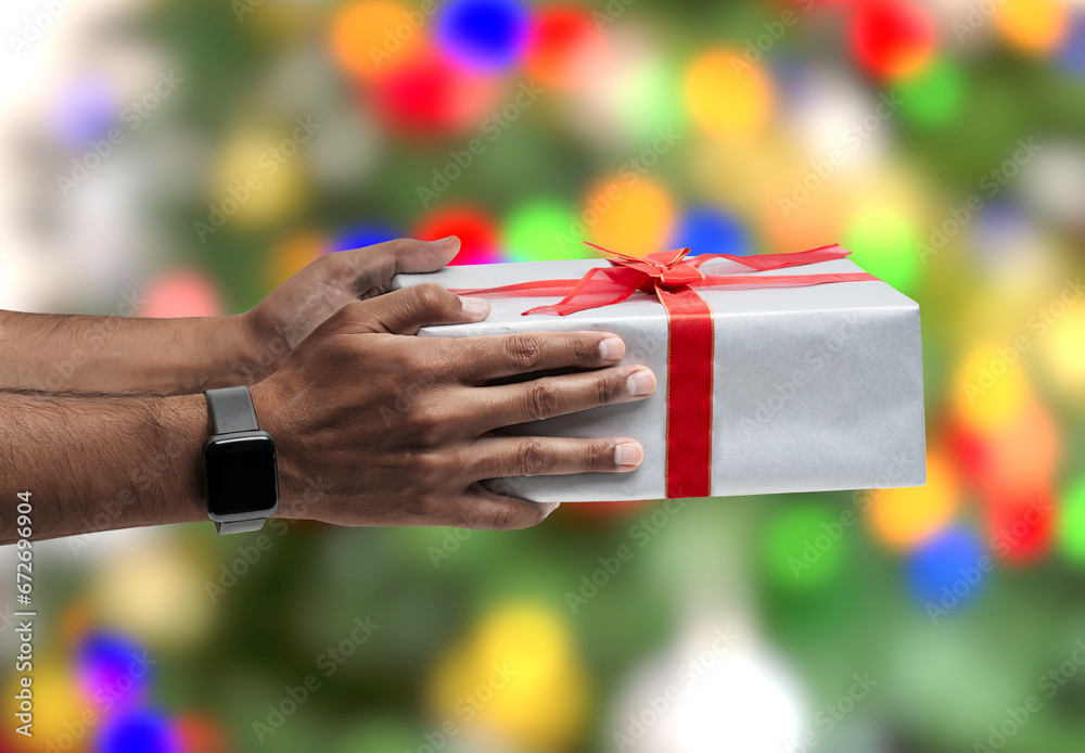 Hand of african young man holding chrismas gift with Christmas tree background