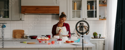 Confident young woman preparing cream for homemade cake and recording video for food blog photo