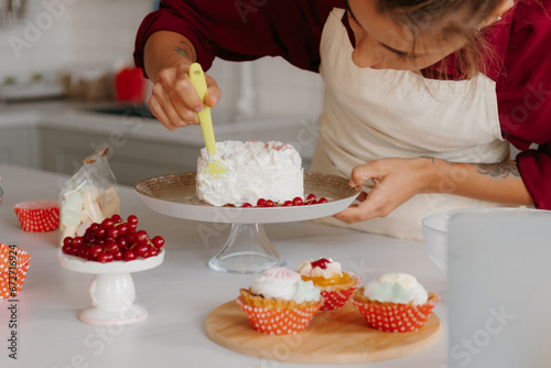 Close-up of skilled female pastry chef applying whipped cream while decorating cake at the domestic kitchen
