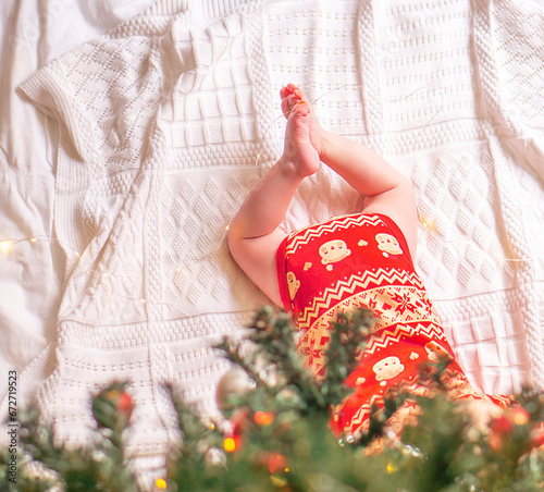 Small baby legs on the blanket under green decorated christmas tree.