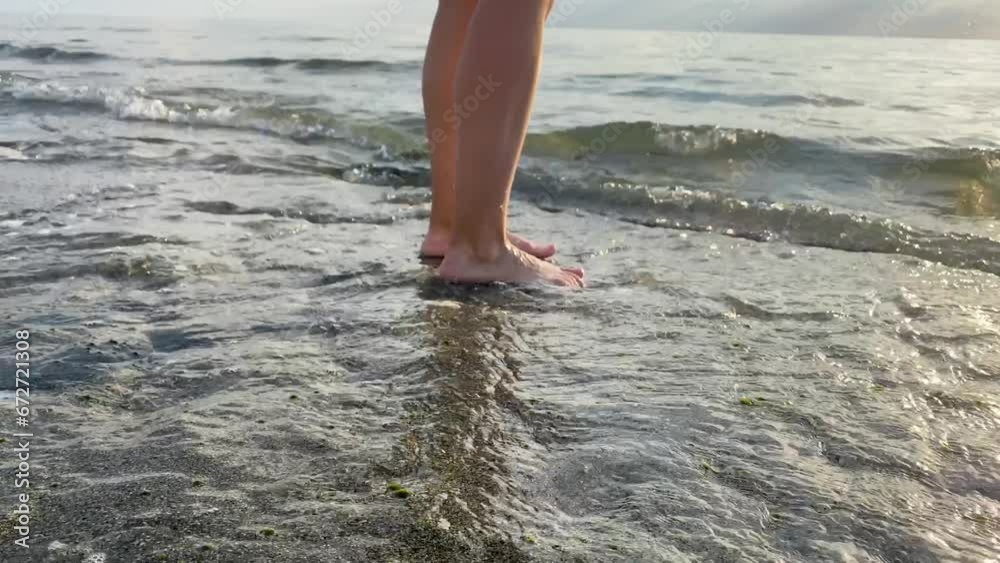 The feet of a teenager stand on the sand and are washed by sea waves . High quality FullHD footage The feet of a teenager stand on the sand and are washed by sea waves . High quality FullHD footage