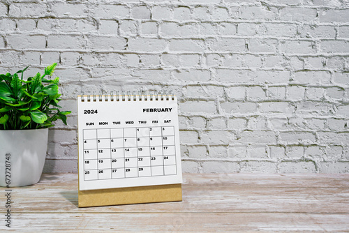 White February 2024 calendar on office wooden desk with potted plant.