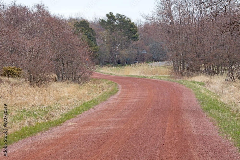 Fototapeta premium The red road at island of Kökar. The bedrock on the island of Kökar is red granite. It is found in road asphalt and gravel roads, Kökar, Ahvenanmaa, Finland.