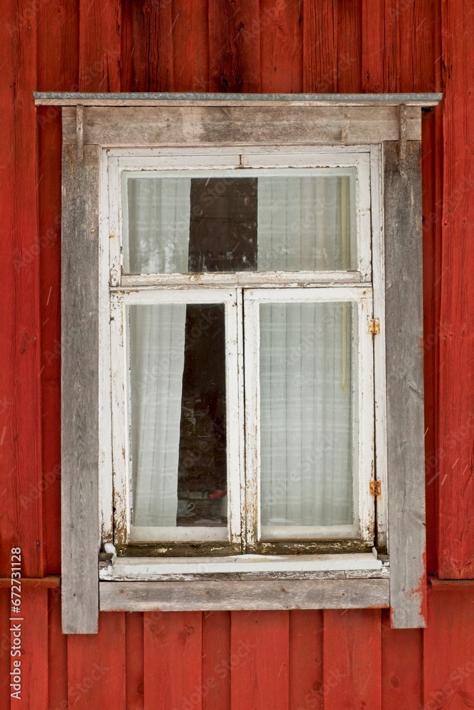 White frame window on the wall of a red painted building.