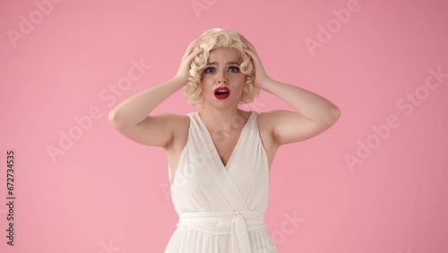 The young woman clutches her head in shock, surprise. The woman nods her head negatively and spreads her hands. A woman in the style of in the studio on a pink background. photo