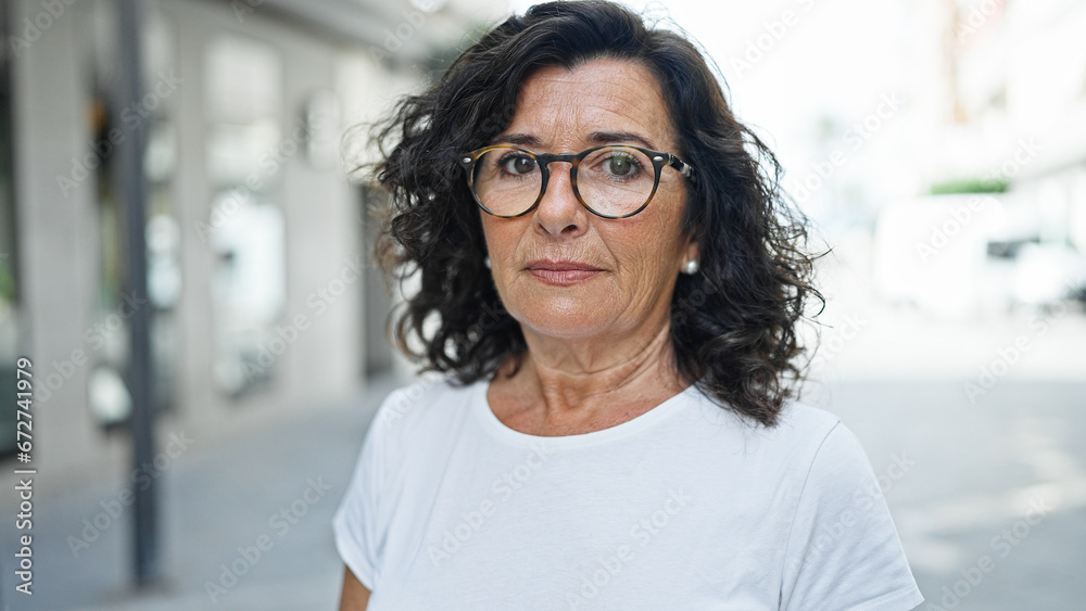 Middle age hispanic woman standing with serious expression at street - obrazy, fototapety, plakaty 