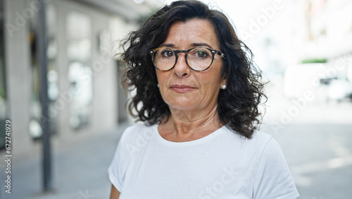Middle age hispanic woman standing with serious expression at street photo