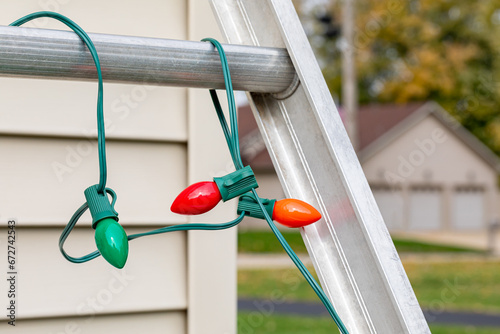 Christmas string lights hanging on ladder rung outside of house. Holiday lighting decorating, ladder safety and accident prevention concept. photo