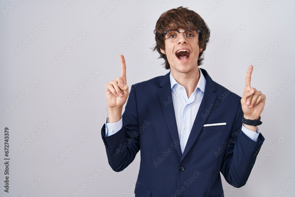Hispanic business young man wearing glasses smiling amazed and surprised and pointing up with fingers and raised arms. Hispanic business young man wearing glasses smiling amazed and surprised and pointing up with fingers and raised arms.