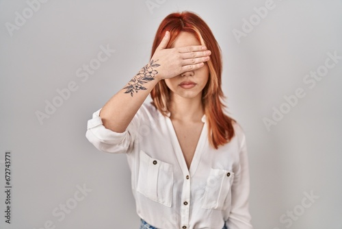 Young caucasian woman standing over isolated background covering eyes with hand, looking serious and sad. sightless, hiding and rejection concept