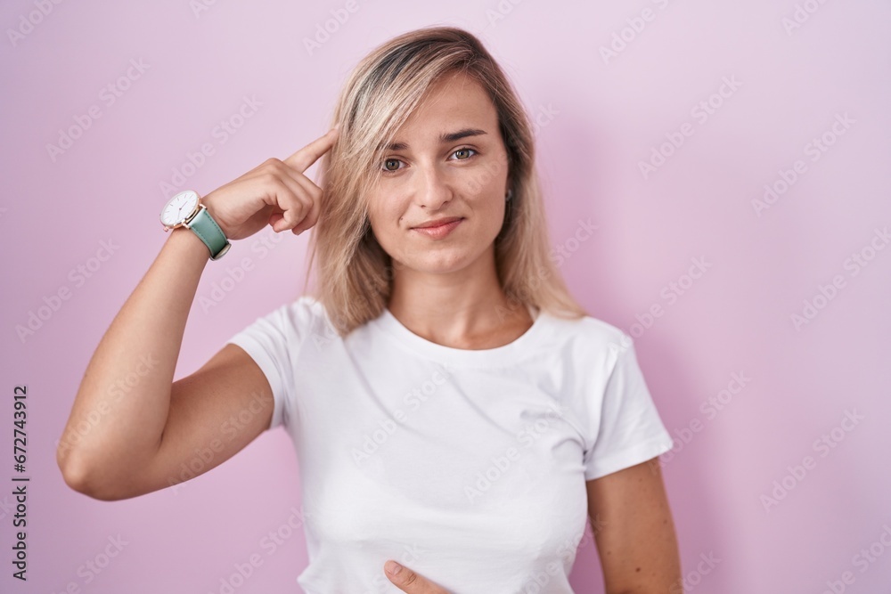 Young blonde woman standing over pink background smiling pointing to head with one finger, great idea or thought, good memory Young blonde woman standing over pink background smiling pointing to head with one finger, great idea or thought, good memory