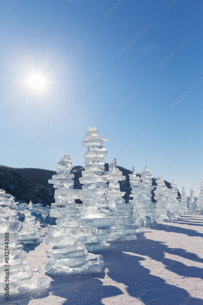 Baikal Lake on cold sunny winter day. Row of traditional high ice pyramids made of transparent ice floes left by tourists near famous Cape Khoboy on Olkhon Island. Winter travel and outdoor recreation