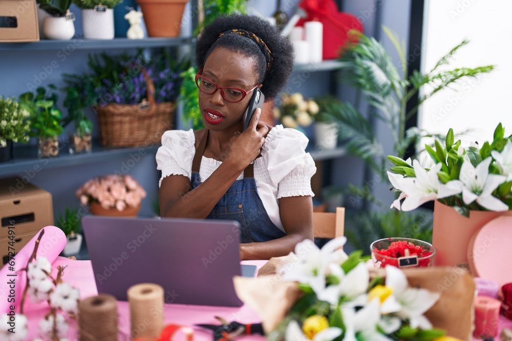 African american woman florist talking on smartphone using laptop at florist store