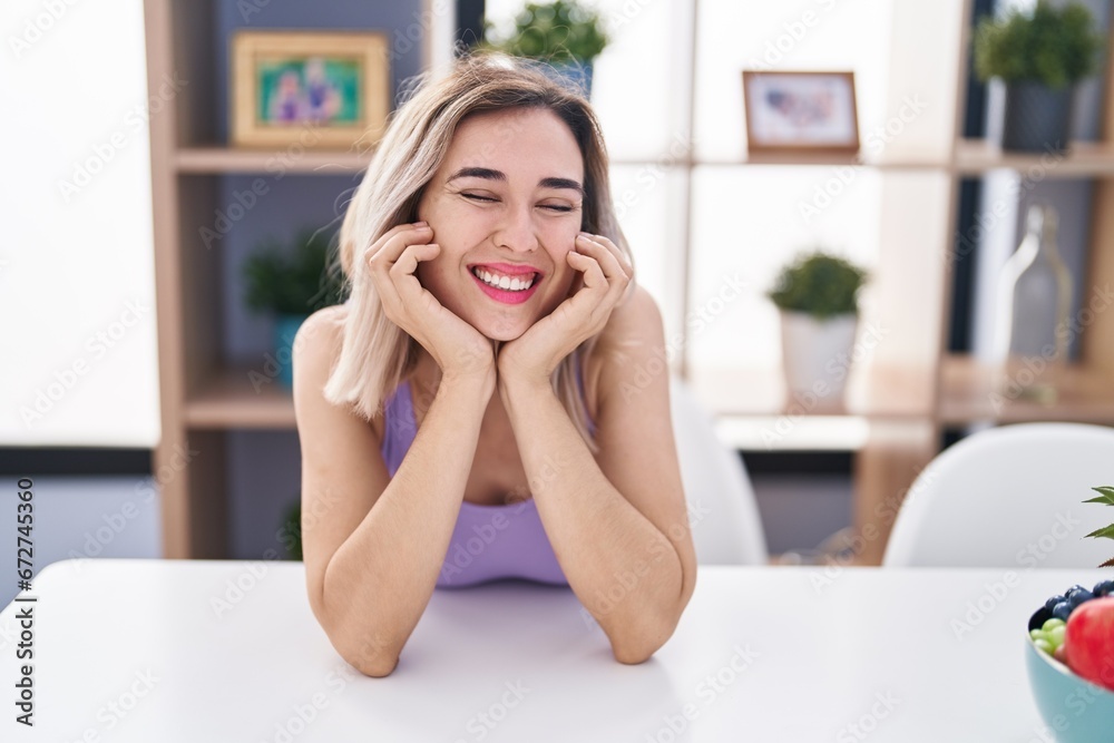Young woman smiling confident sitting on table at home Young woman smiling confident sitting on table at home