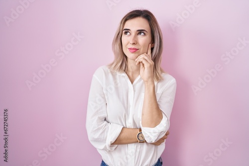 Young beautiful woman standing over pink background with hand on chin thinking about question, pensive expression. smiling with thoughtful face. doubt concept.
