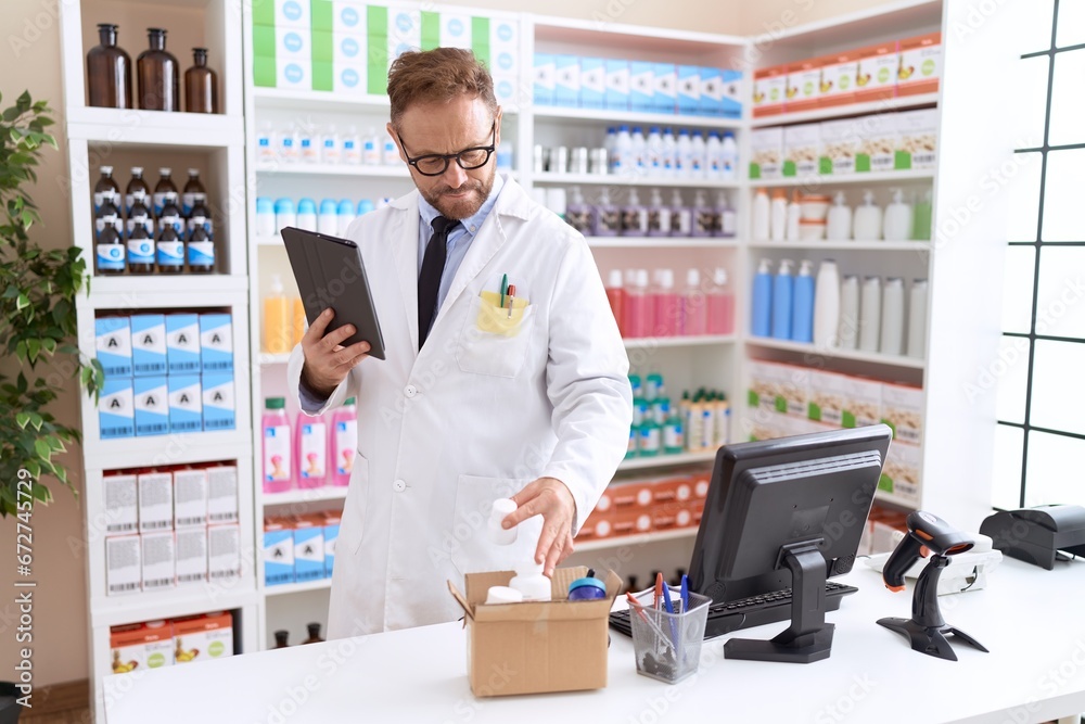 Middle age man pharmacist using touchpad holding pills bottle at pharmacy Middle age man pharmacist using touchpad holding pills bottle at pharmacy