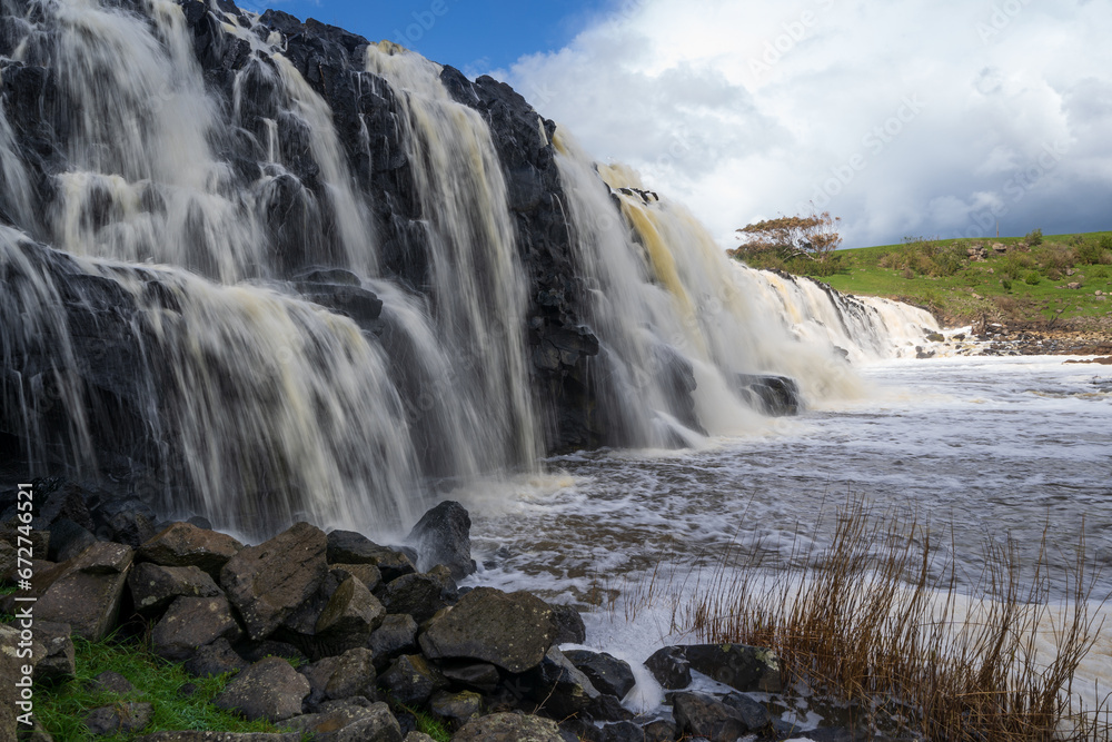 Close up view of a wide rocky waterfall with dramatic storm clouds above Close up view of a wide rocky waterfall with dramatic storm clouds above