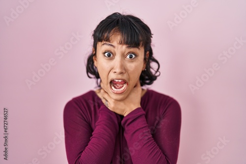 Young beautiful woman standing over pink background shouting and suffocate because painful strangle. health problem. asphyxiate and suicide concept.