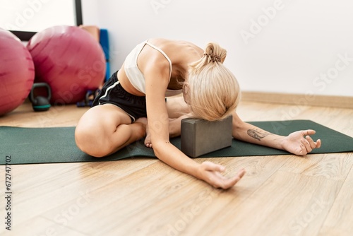 Young blonde woman training yoga exercise with head on block at sport center