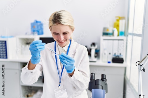 Young blonde woman scientist pouring liquid on sample at laboratory