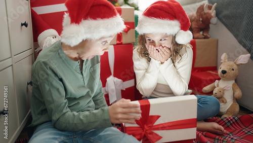 Obraz na plátně Two kids unpacking gift sitting on floor by christmas tree at home