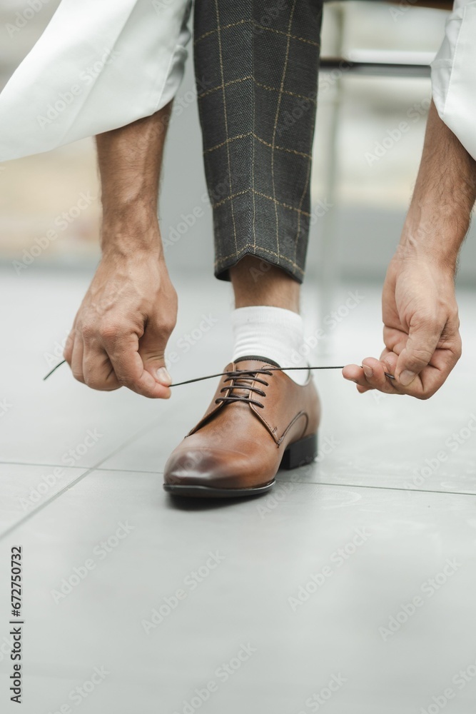 Closeup of the hands of a person tying shoelace of his brown leather shoes