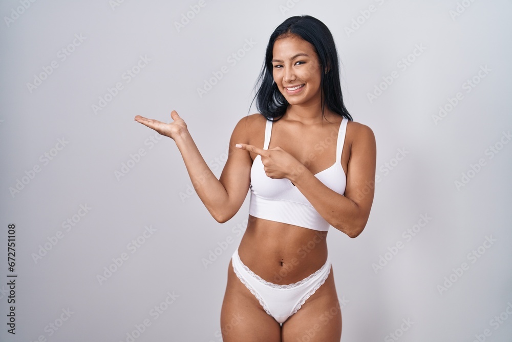 Hispanic woman wearing lingerie amazed and smiling to the camera while presenting with hand and pointing with finger. Hispanic woman wearing lingerie amazed and smiling to the camera while presenting with hand and pointing with finger.