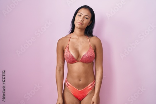 Hispanic woman wearing bikini relaxed with serious expression on face. simple and natural looking at the camera.