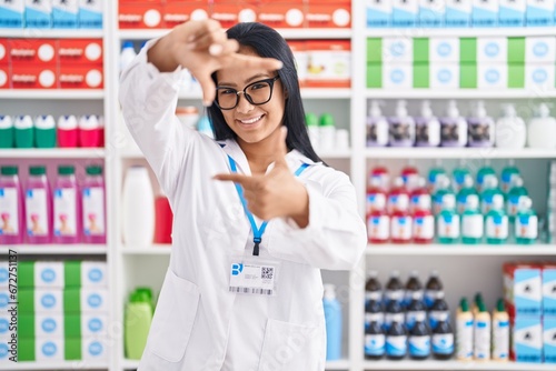 Hispanic woman working at pharmacy drugstore smiling making frame with hands and fingers with happy face. creativity and photography concept.